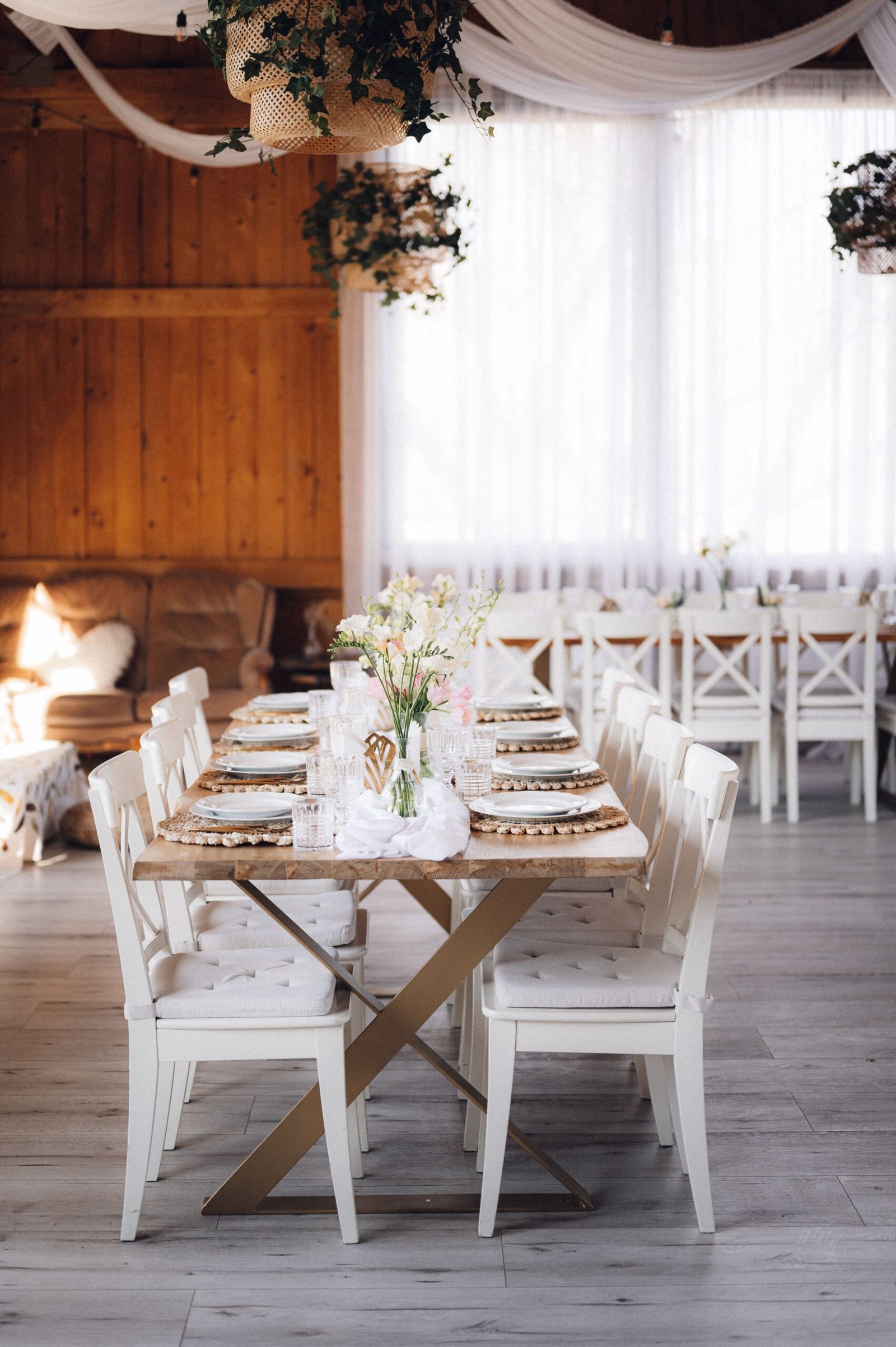 An interior of restaurant with wedding table and white chairs adorned with flowers