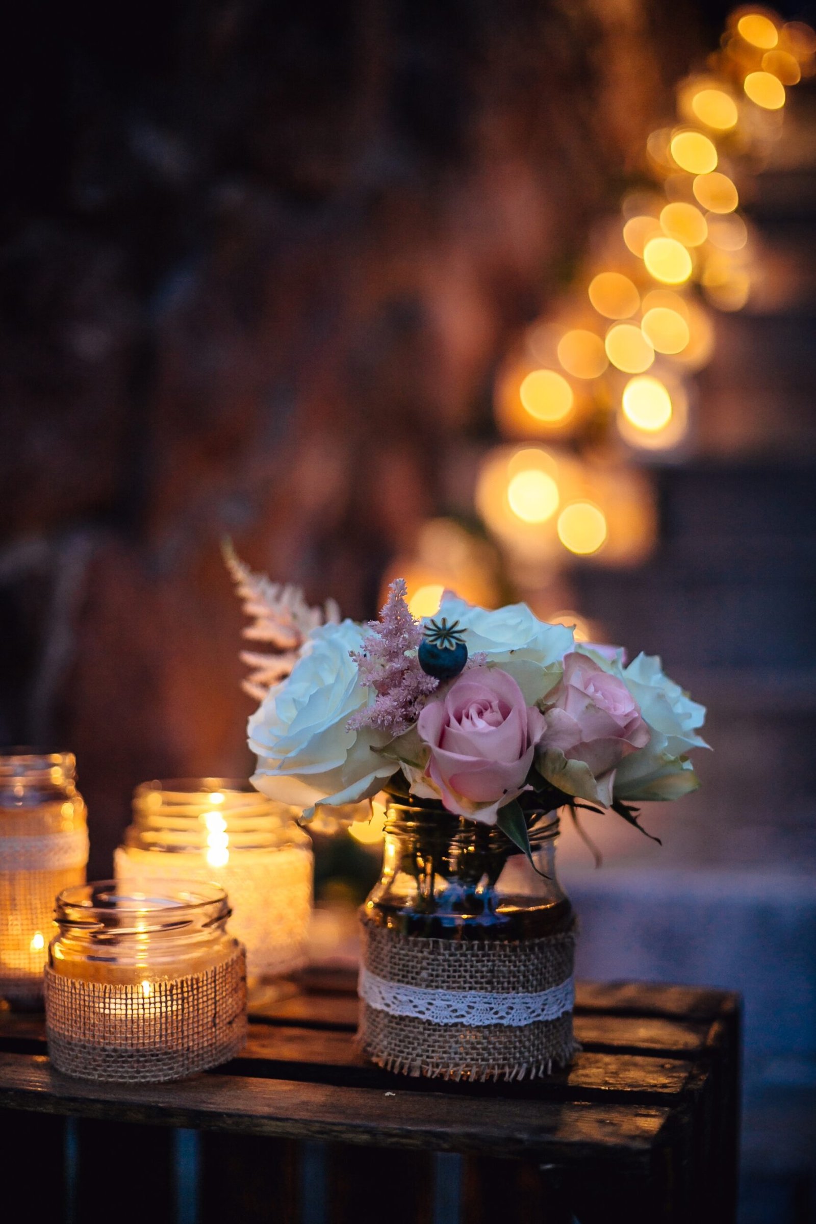 A vertical closeup shot of a small bouquet in a vase and candle jars on a wooden table